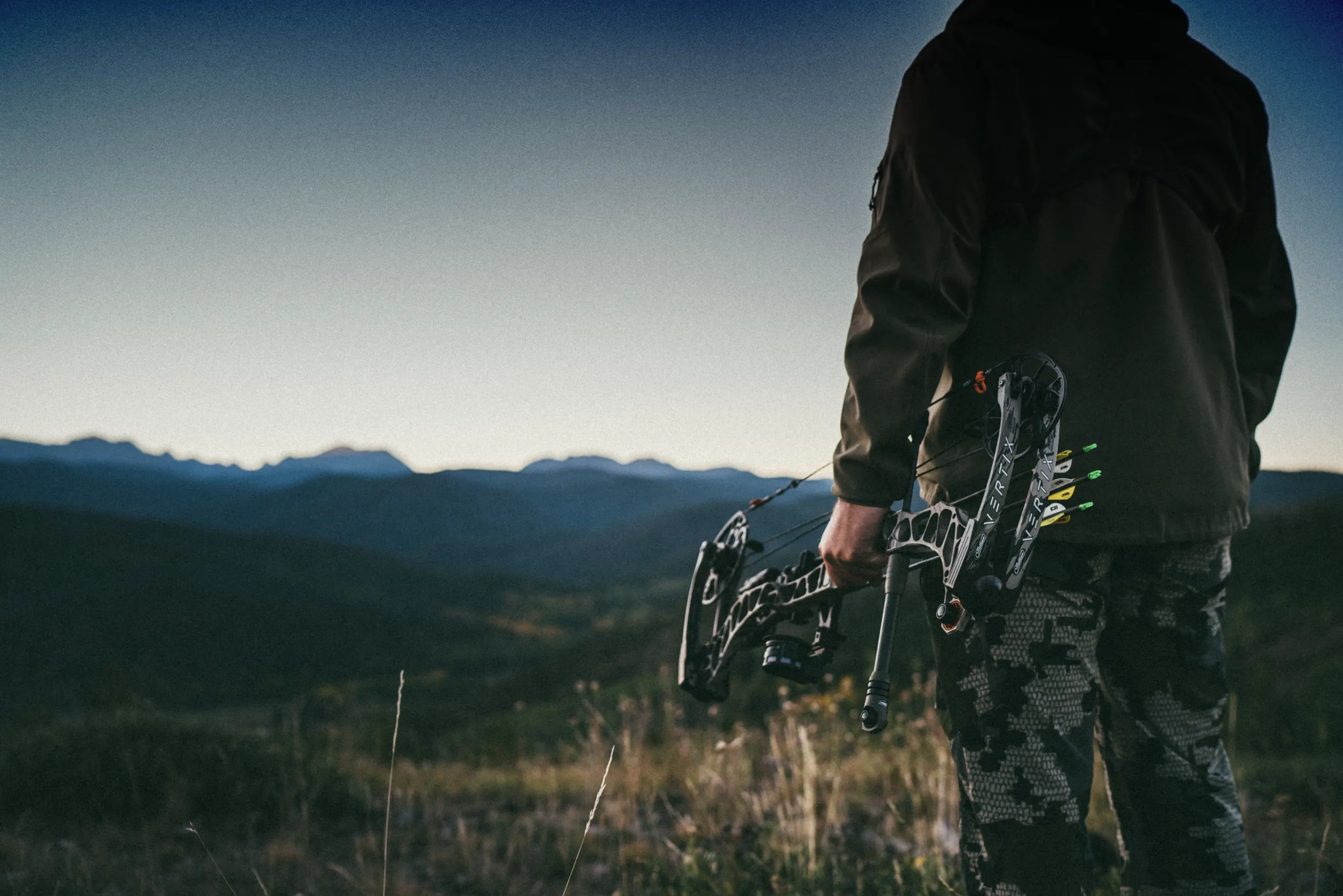 A hunter holds his crossbow while gazing out over the landscape